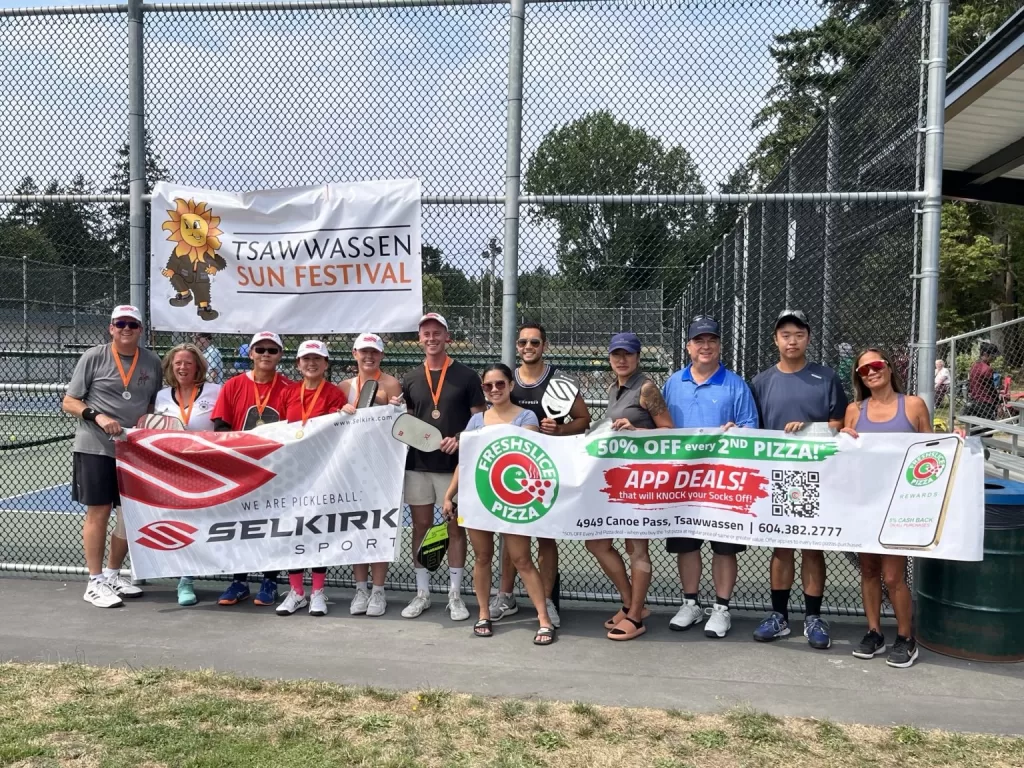 People holding banners for Freshslice Pizza and Selkirk Sports at the Tsawwassen Sun Festival