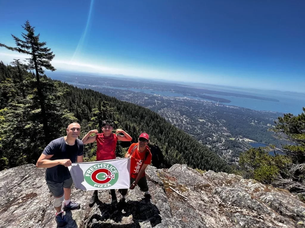 Freshslice Pizza HQ team holding Freshslice Pizza banner at top of Grouse Grind in Vancouver